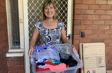 Person preparing for a HomeCycle pick up, holding box of clothes and cardboard for recycling.